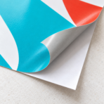 Coin d’un vinyle imprimé soulevé pour montrer sa face adhésive et le papier support blanc.
